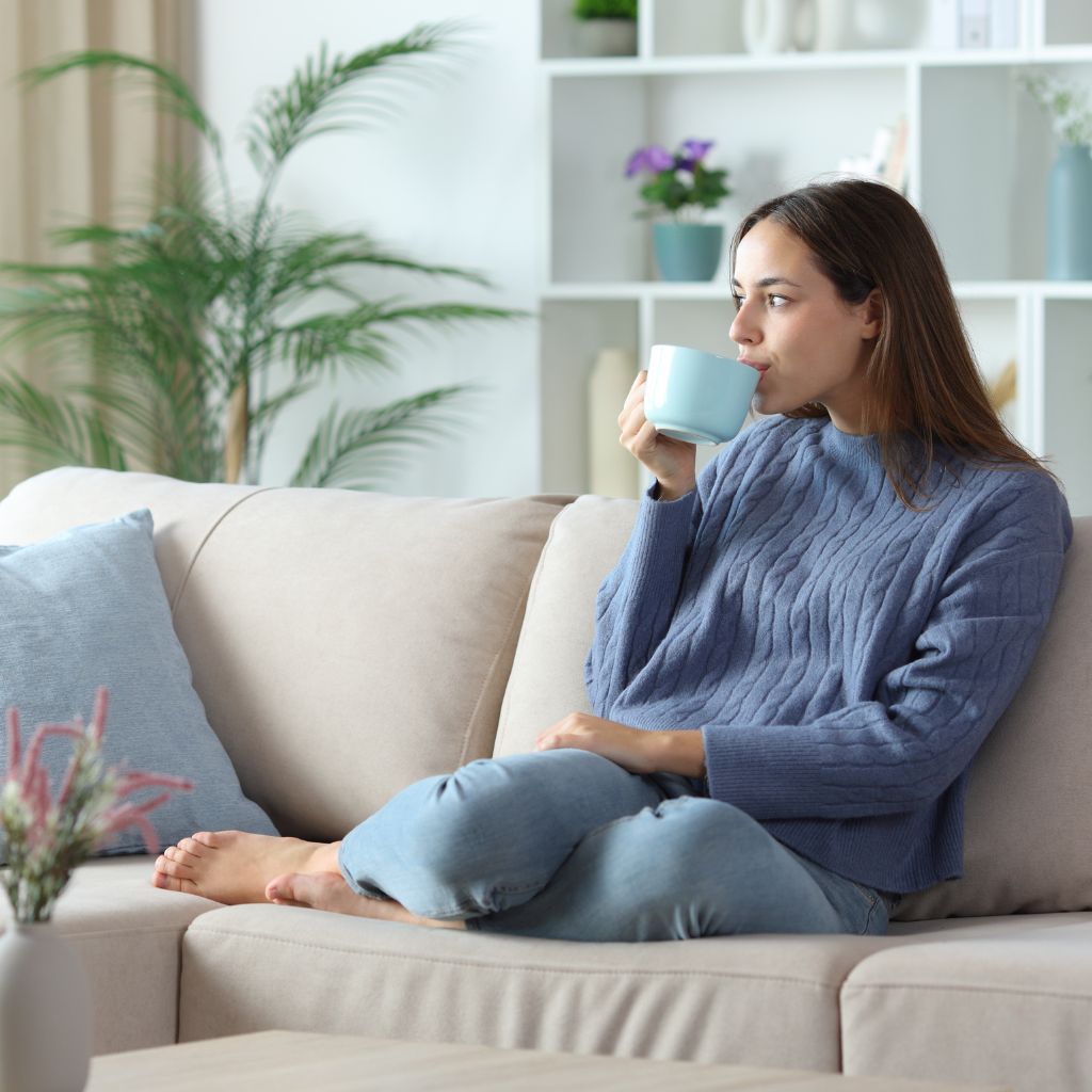 Frau, die zu Hause auf einem Sofa sitzt und Kaffee oder Tee trinkt.
