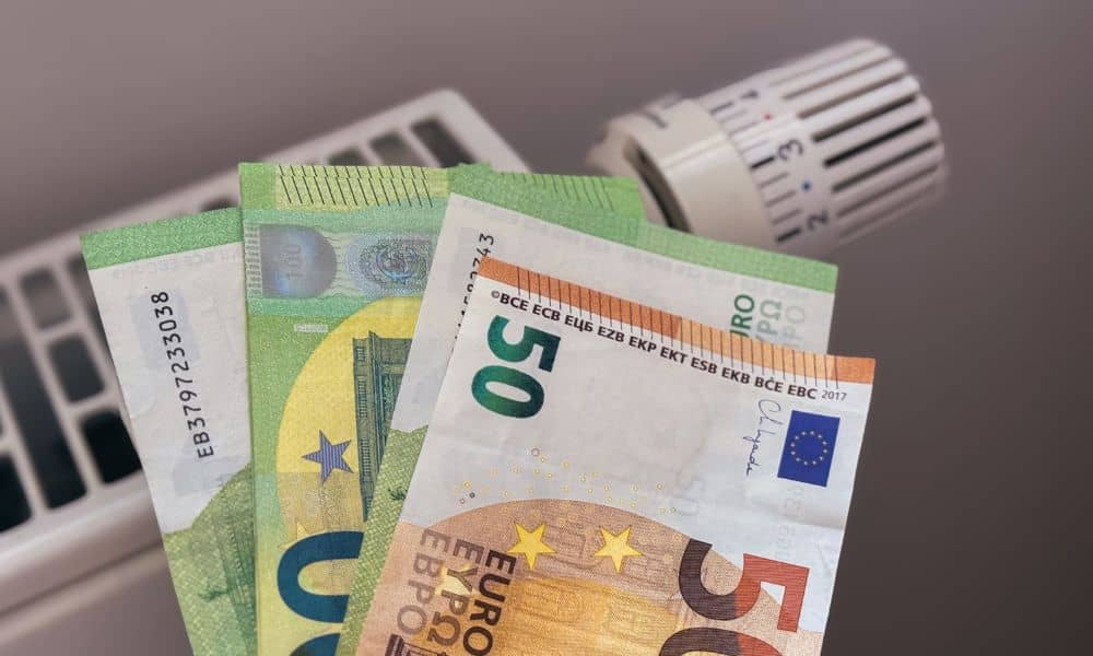 Hand hält Euro‑Banknoten vor einen Heizkörper zu Hause