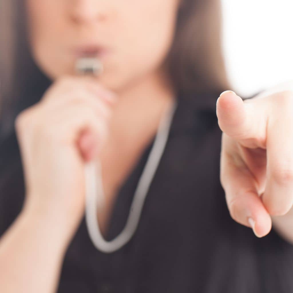 Frau zeigt mit dem Finger auf den Betrachter und bläst in eine Schiedsrichterpfeife