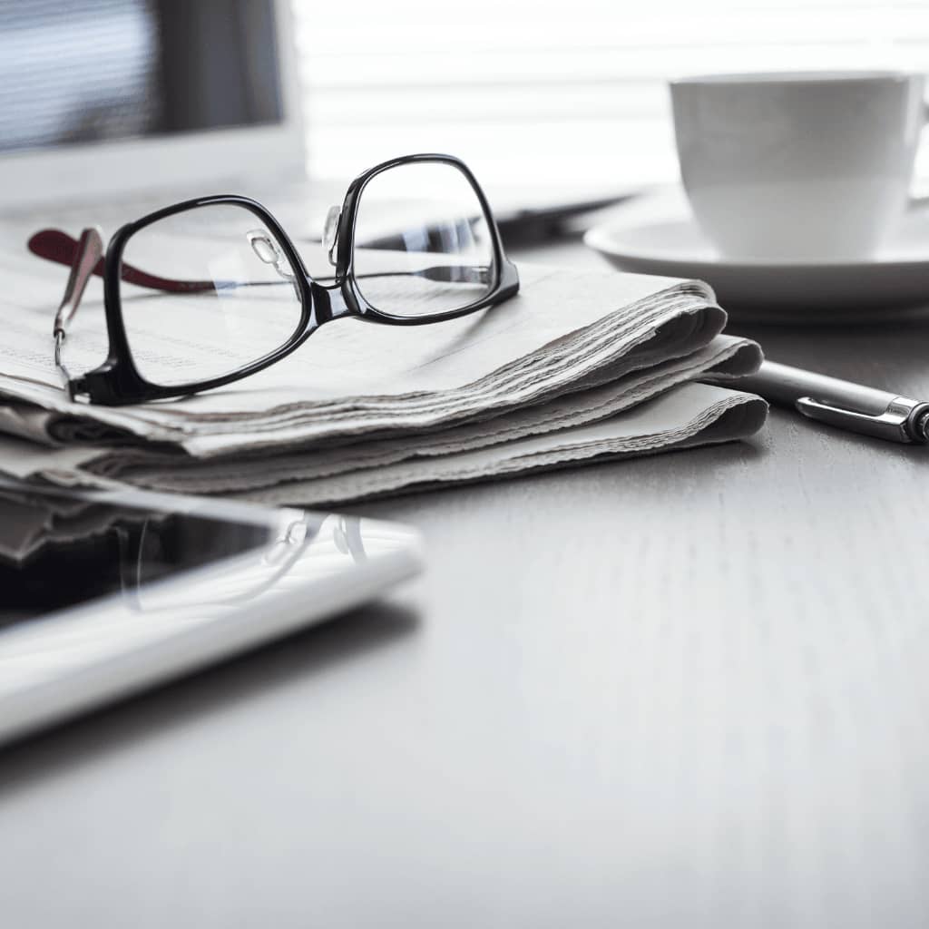 Brille liegt auf Zeitung, daneben eine Tasse