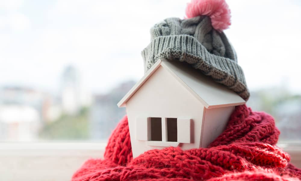 Das Modell eines Holzhäuschens ist warm eingepackt in Mütze und Schal.