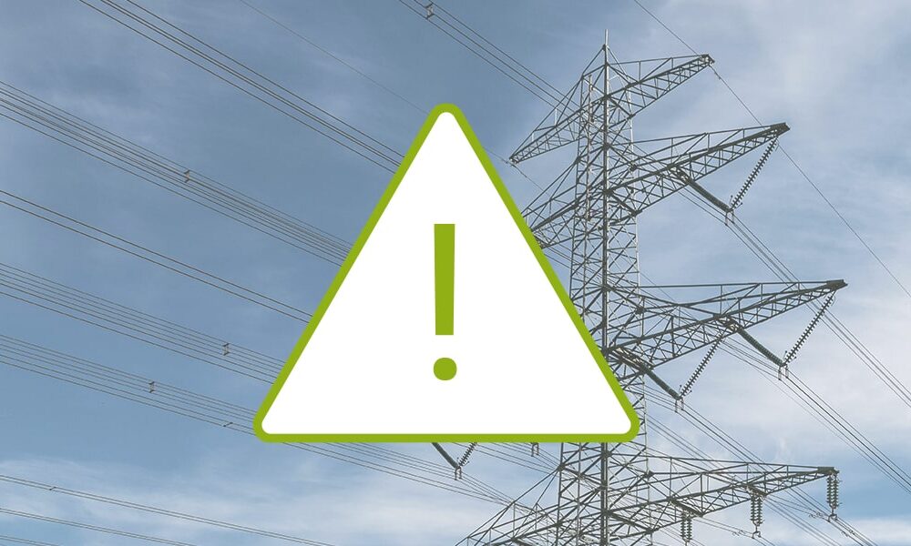Strommast vor blaugrauem Himmel, aufgesetztes grünes Warndreieck mit Ausrufezeichen, Störung